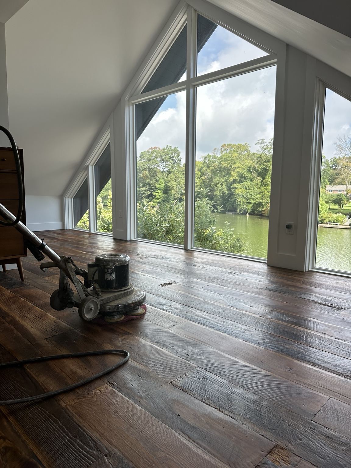 Professional floor machine on a dark varied-tone wood floor beside large windows