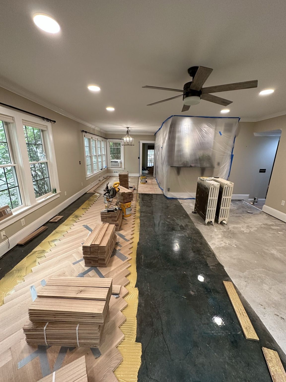 Herringbone boards being laid over the leveled substrate, with the dark adhesive bed visible down the room