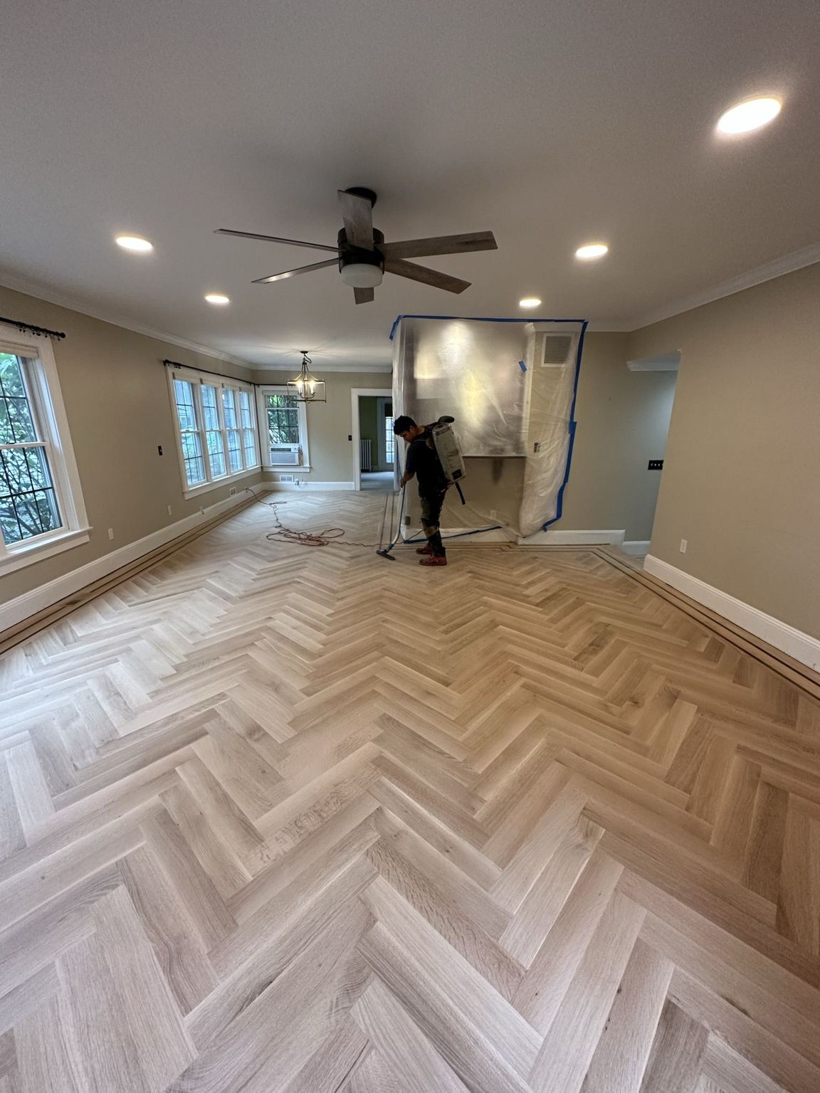 Unfinished herringbone field fully installed, being sanded with dust containment on the walls