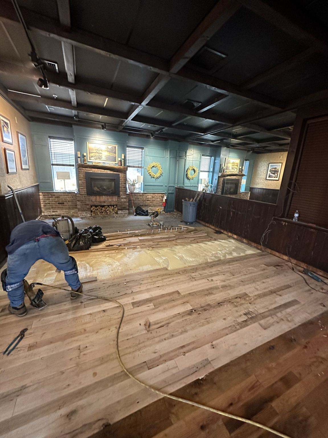 Crew member installing reclaimed hardwood boards over the new subfloor