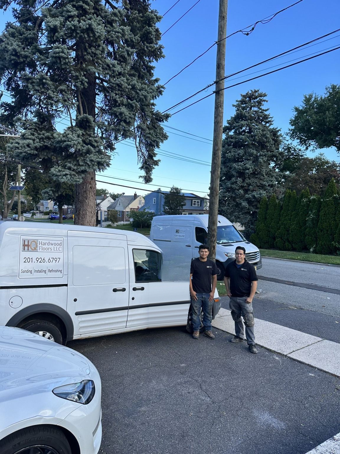 HQ Hardwood Floors crew standing with the company's lettered work vans