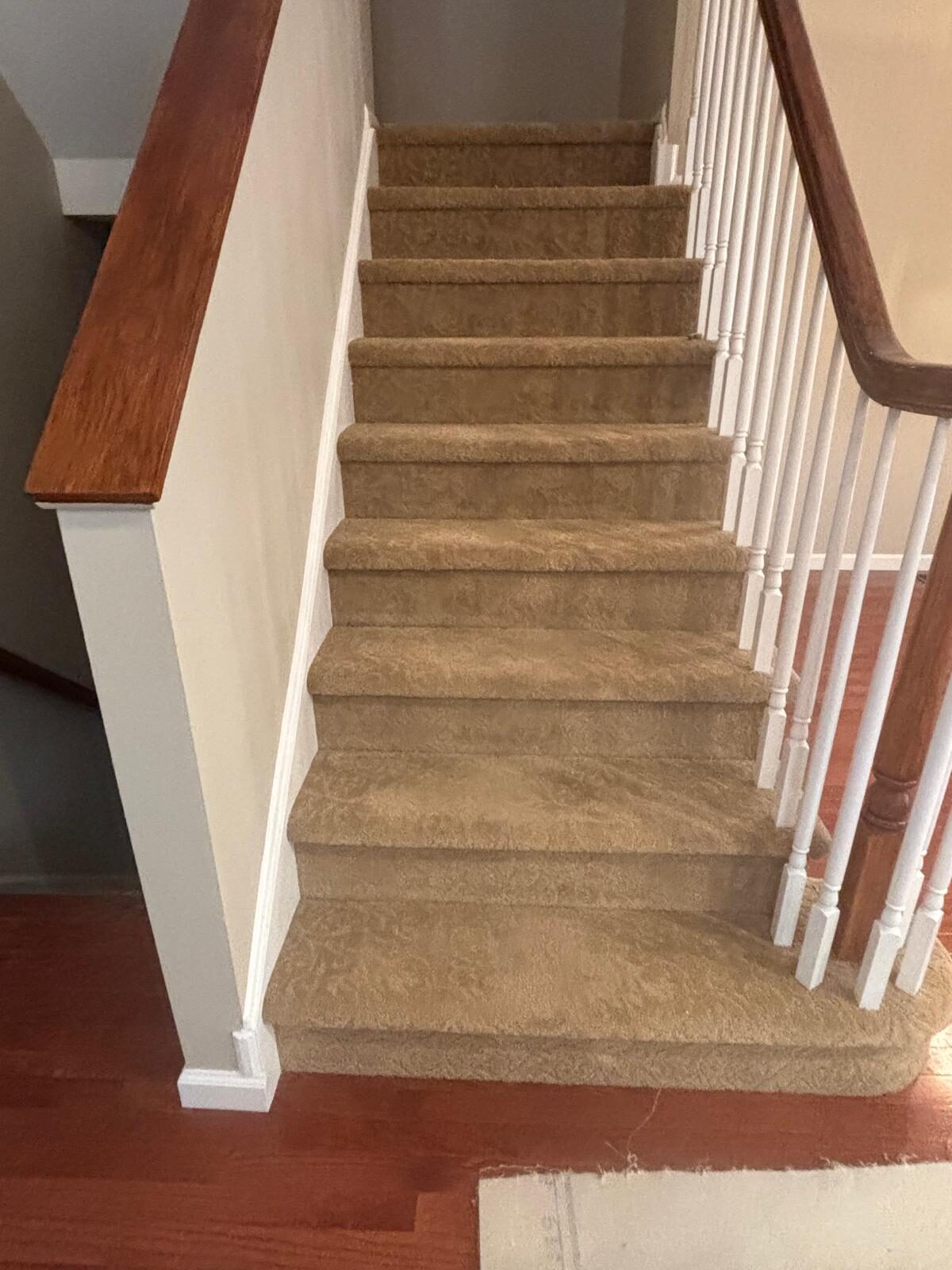 Carpeted staircase with white balusters and a wood handrail, before the carpet was removed