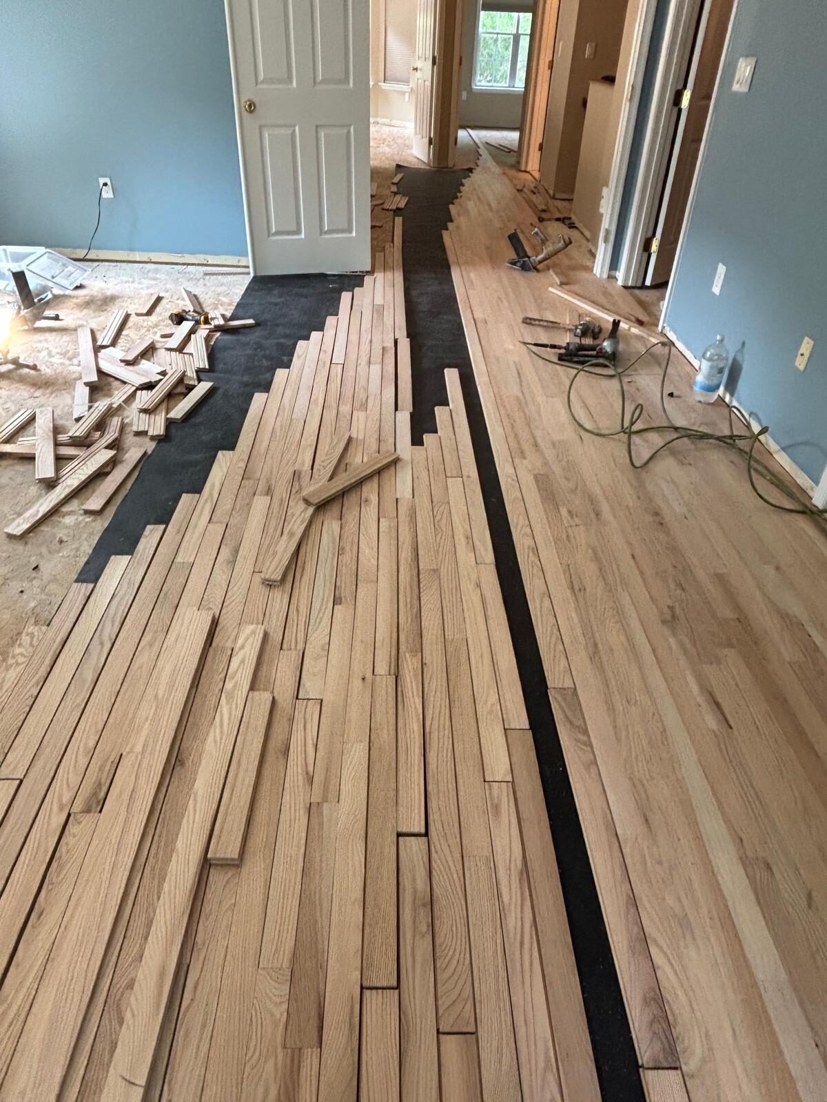 Unfinished red oak strip flooring being installed over black underlayment paper in an upstairs hallway